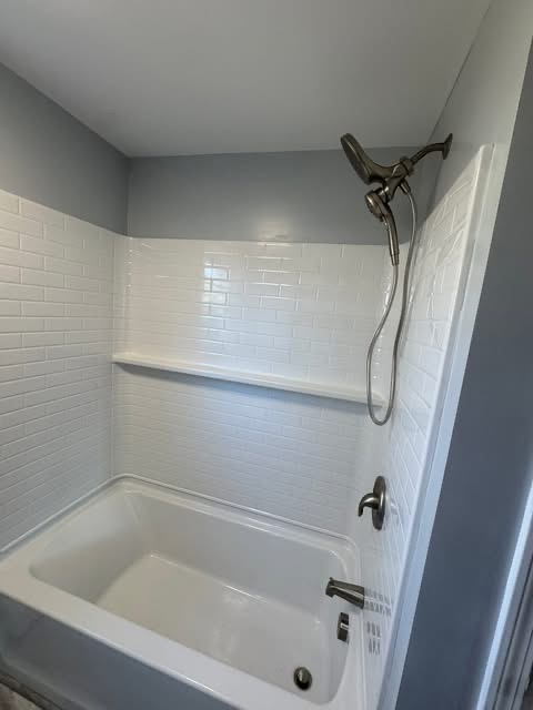 New tub with a tiled surround, corner shelf, and matte-black rainhead + handheld combo.