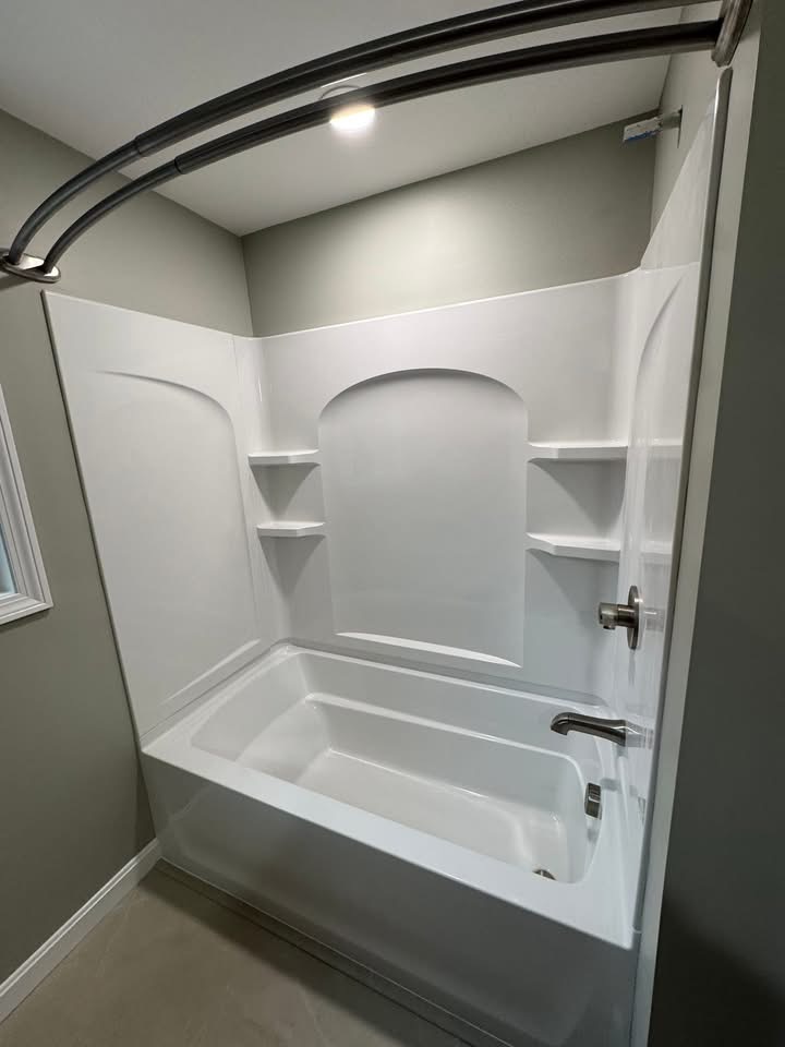 New soaking tub with a sculpted tub/shower surround and matte-black curved rod.