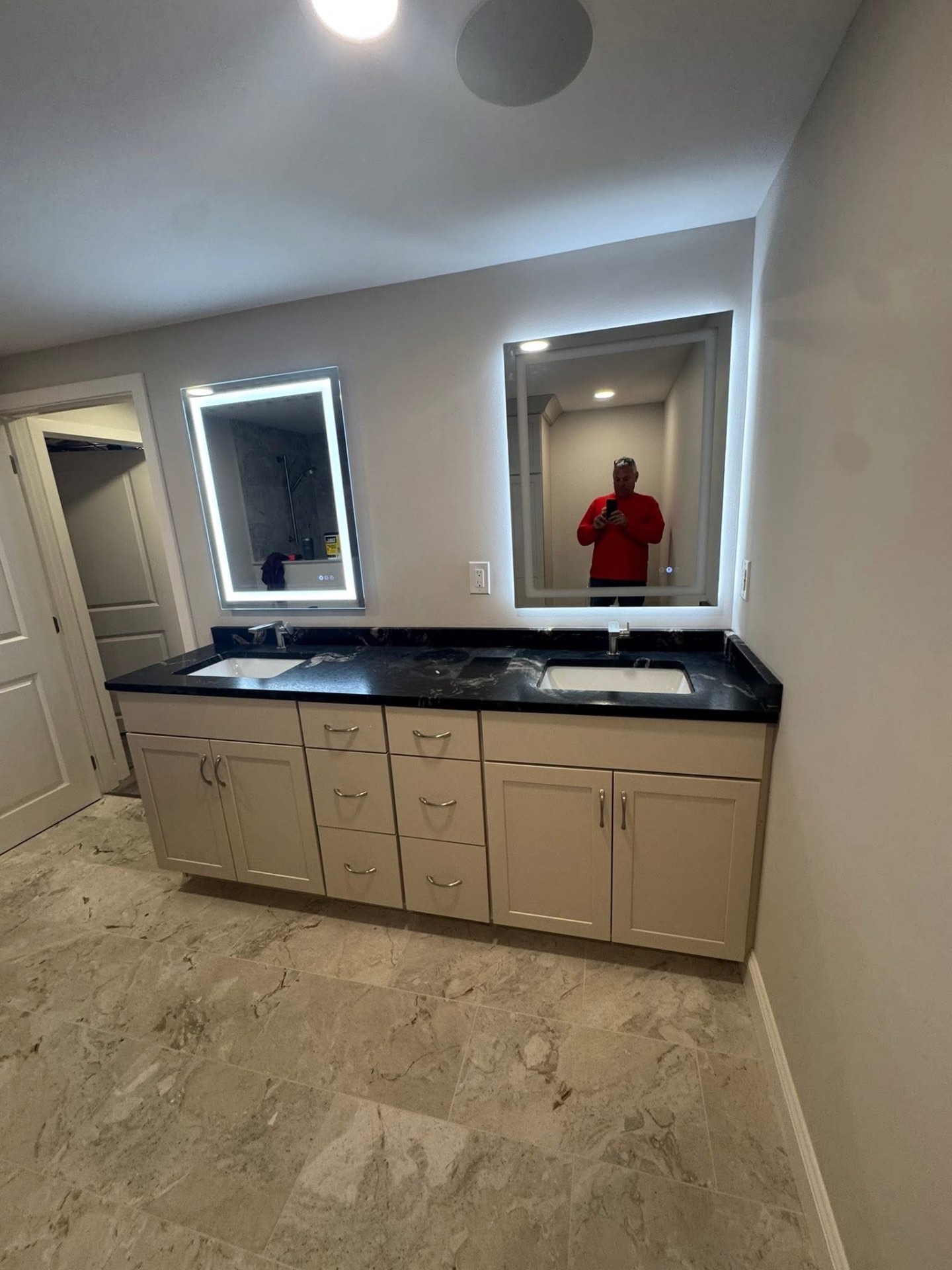 Double-sink vanity with taupe shaker cabinets, black quartz counter, and backlit LED mirrors.