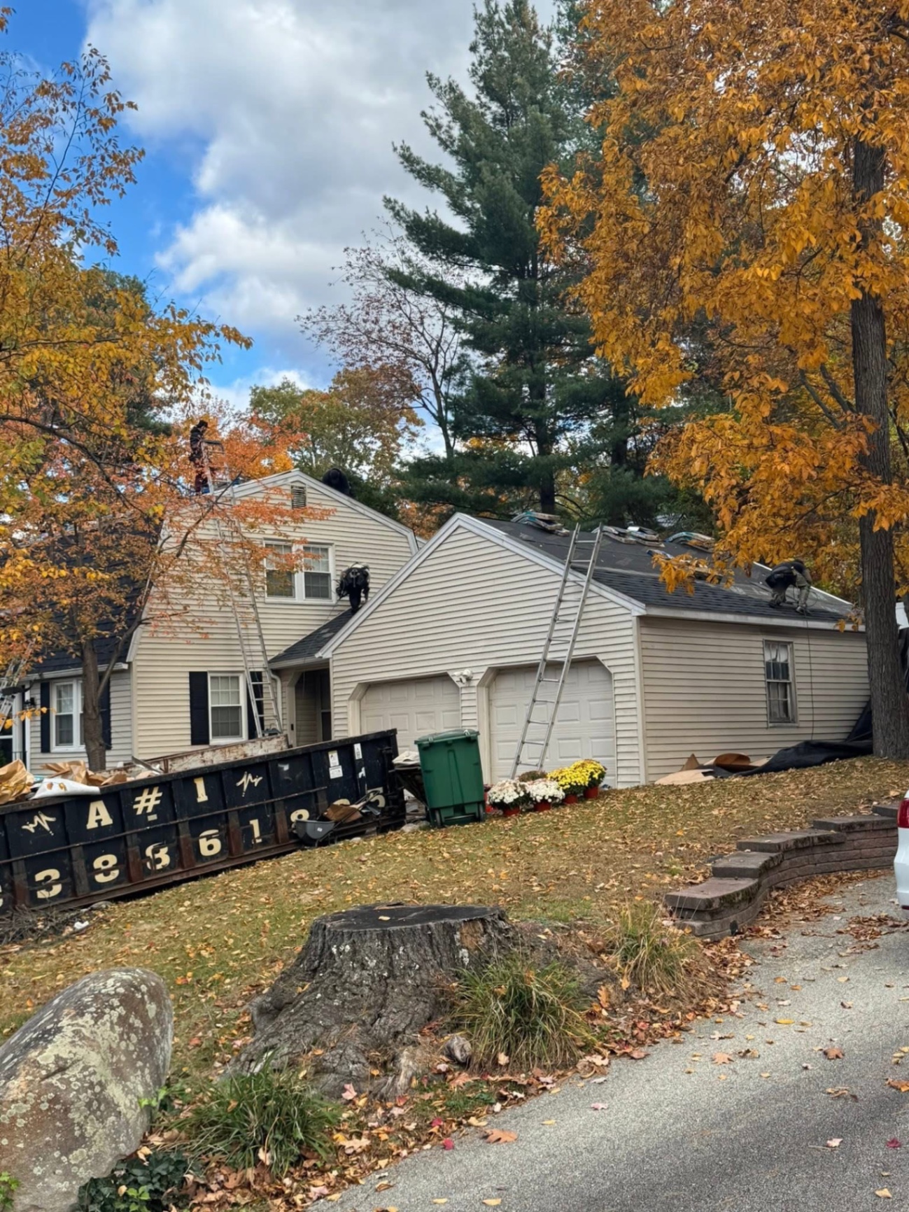Tear-off day — crew stripping the old shingles off the main house, dormer, and garage with the dumpster staged on the lawn.