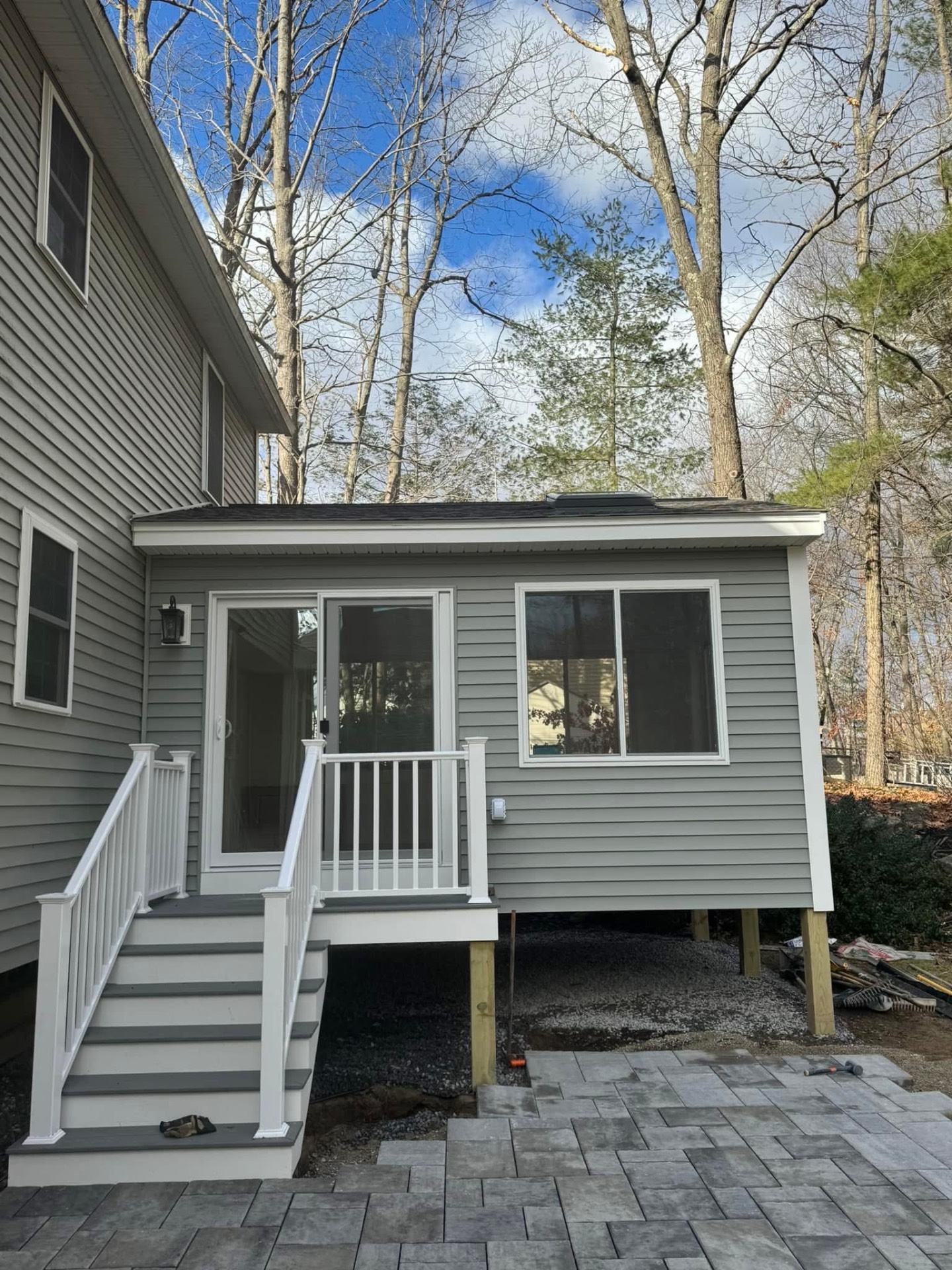Front view — glass slider door, white staircase, and paver patio leading down from the addition.