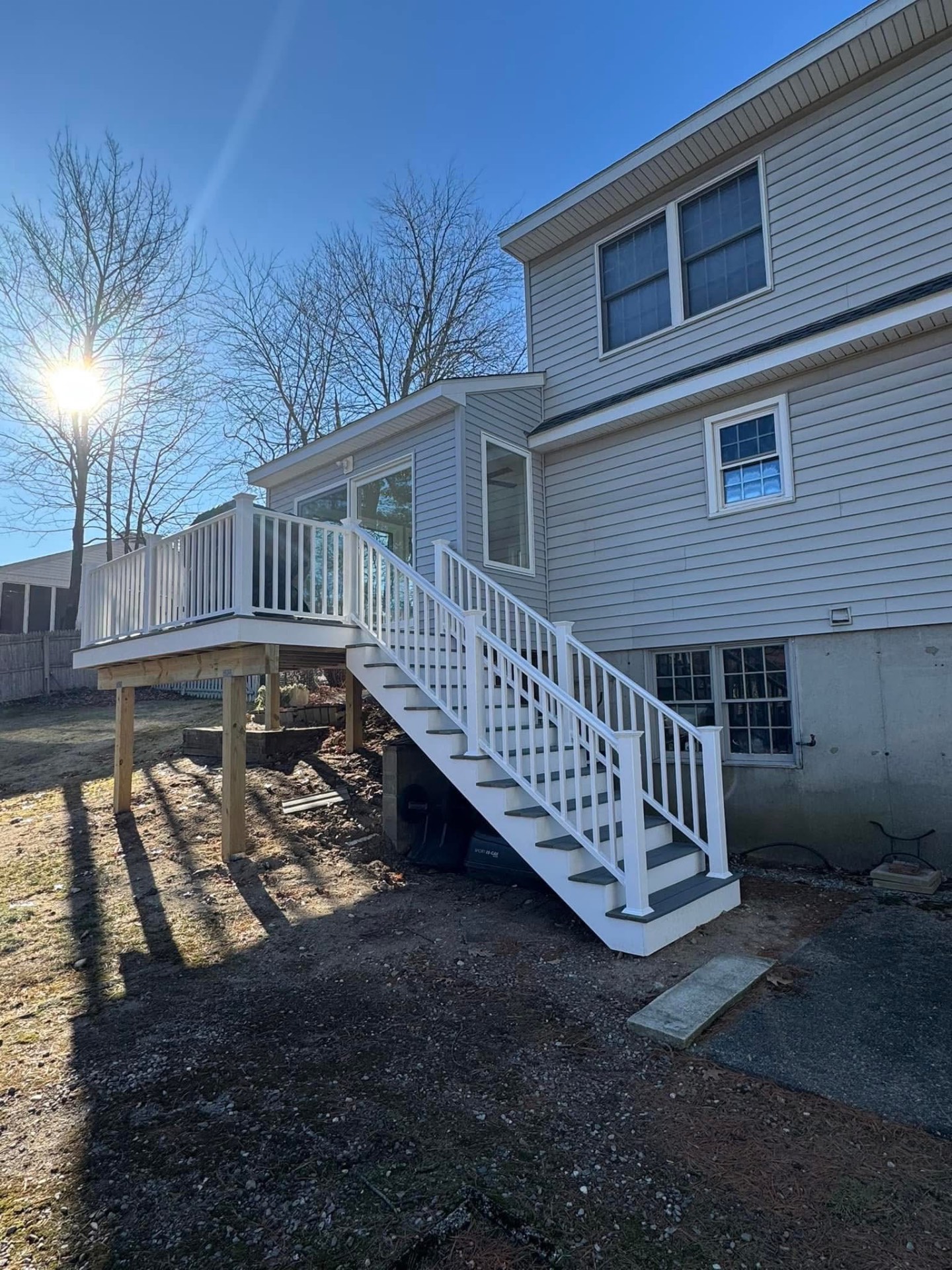Side view of the finished elevated deck: white vinyl railings, wrapped fascia, and full stair run down to grade.