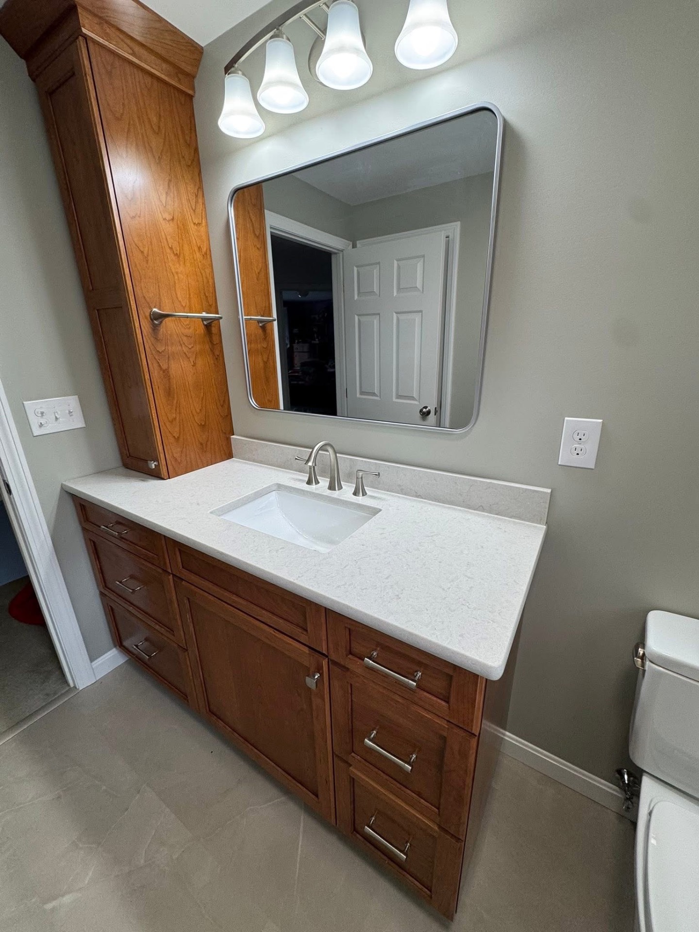 Custom cherry vanity and linen tower with quartz counter, undermount sink, and brushed-nickel fixtures.