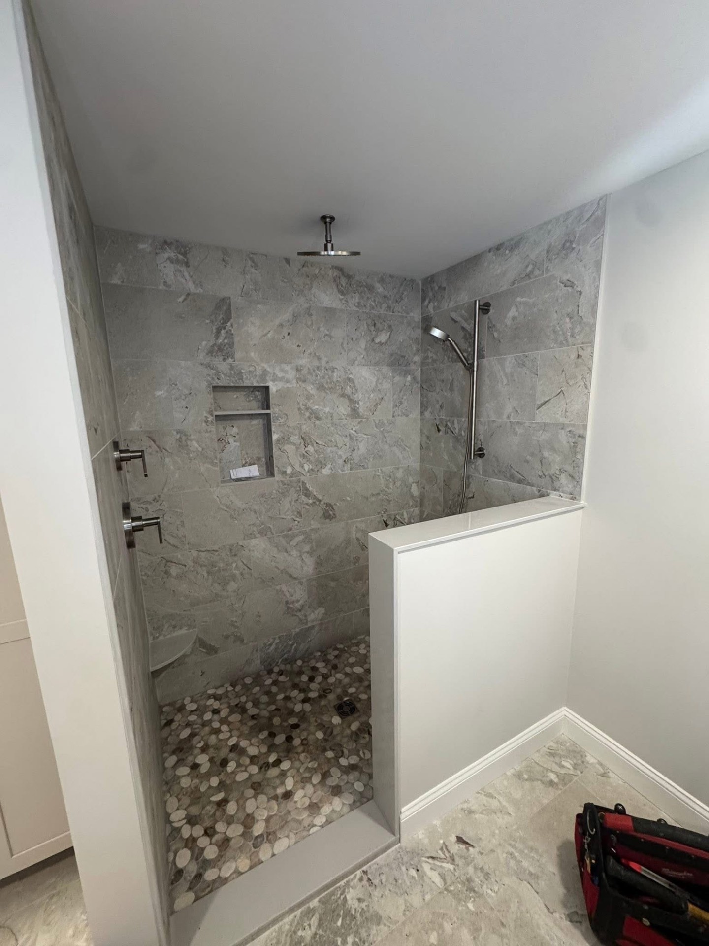New 3/4 bath with a fully tiled walk-in shower, pebble floor, niche, and matte-black rainhead fixture.