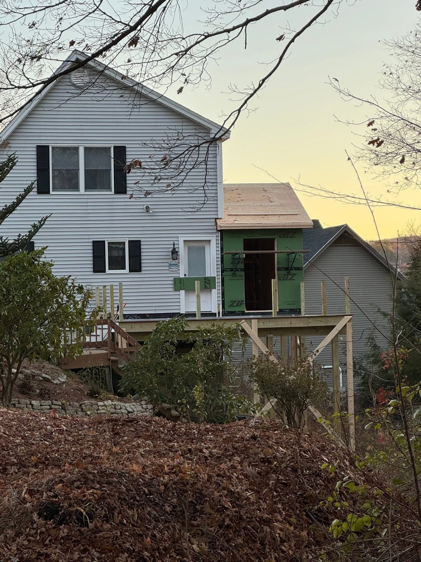 Deck & mudroom — dusk shot showing the new deck, stairs, and framed mudroom addition tied into the back of the home.