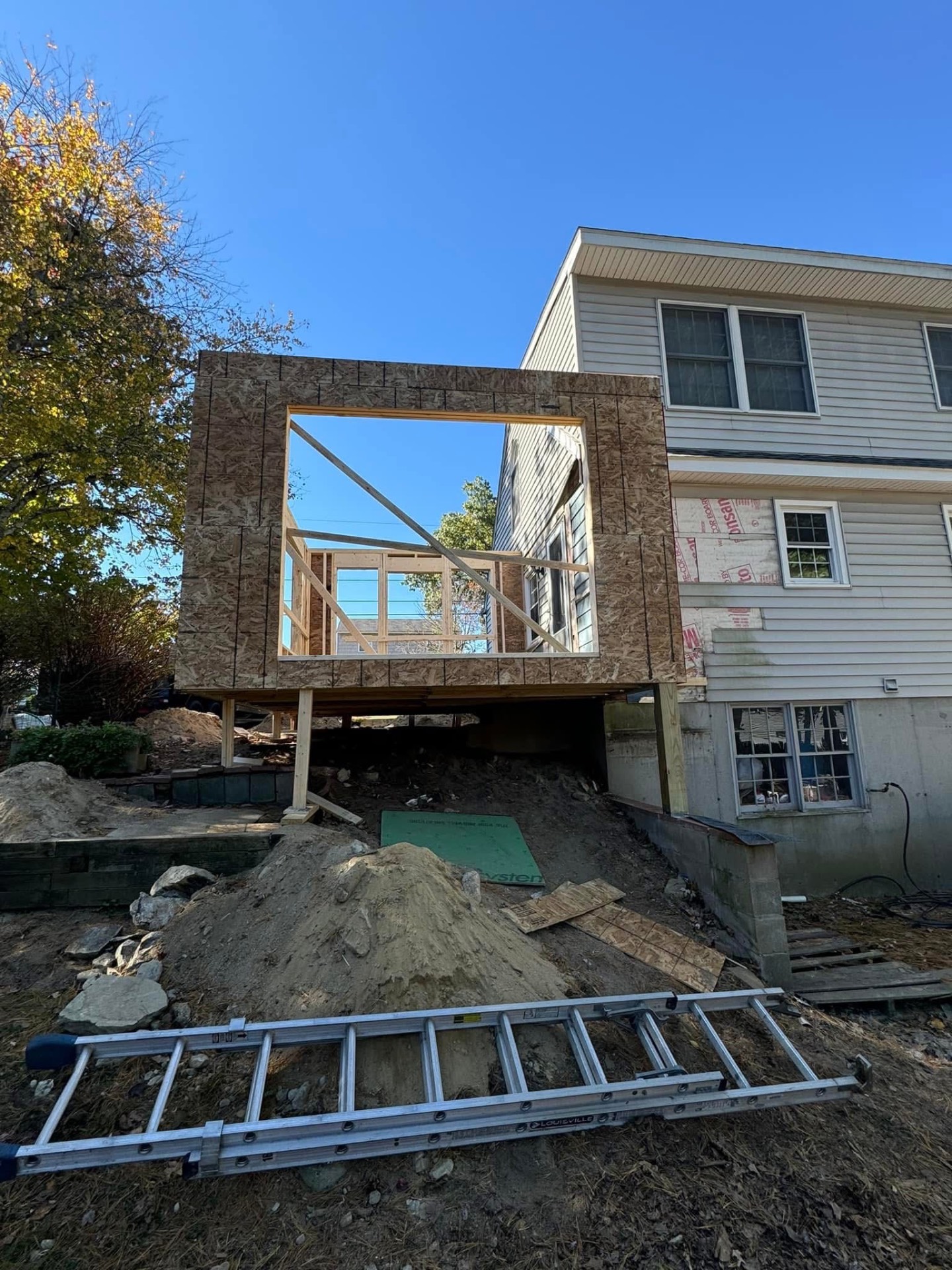 Rear addition — new two-story bump-out sheathed and standing on pressure-treated posts over concrete piers.