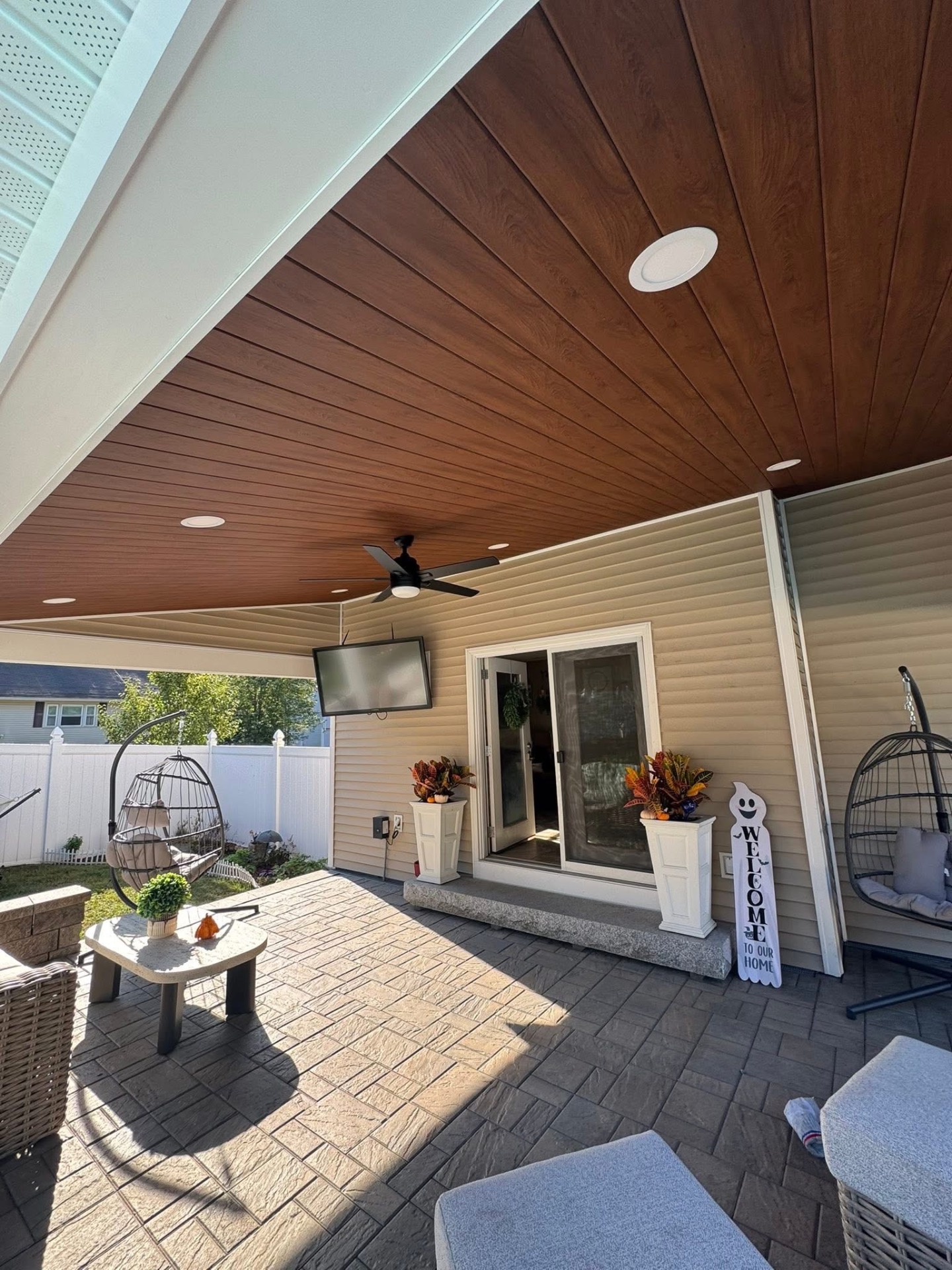 Stained wood-look tongue-and-groove porch ceiling with recessed lighting and a ceiling fan over the seating area.